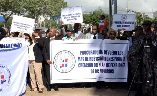 **Cambio de Noticia: Marcha del Colegio Dominicano de Notarios Exige Fondos Retenidos por la Procuraduría** En un acto de reclamo, miembros del Colegio Dominicano de Notarios marcharon hacia la Procuraduría General de la República, exigiendo la entrega de más de 113 millones de pesos que alegan la entidad retiene de forma "ilegal e injustificada", afectando al gremio. La presidenta del Colegio, Laura Sánchez Jiménez, lideró la manifestación, explicando que la entidad busca la aplicación de la Ley 140-15 para asegurar planes de pensiones, ayudas médicas y contar con recursos necesarios para la firma digital. La marcha, iniciada en la esquina de las avenidas Jiménez Moya con Correa y Cidrón, concluyó en el edificio que alberga la Procuraduría. Sánchez Jiménez sostuvo que la Procuraduría dejó de pagar al Colegio por la transferencia de 130 pesos por cada acto notarial certificado desde la entrada en vigor de la Ley 140-15 en agosto de 2015. Durante este periodo, según la presidenta, la Procuraduría no ha acreditado completamente los montos correspondientes al Colegio, acusándola de causar daños materiales y morales al afectar las labores de la entidad. Señaló que la Procuraduría ha percibido cerca de tres mil millones de pesos por la aplicación del recibo notarial, alegando que la entidad debería cobrar 130 pesos por cada acto notarial según la Ley 140-15 del Notariado, pero está cobrando 700 pesos, entregando solo 80 pesos al Colegio. Además, advirtió que el Colegio Dominicano de Notarios no permitirá transgresiones ni actuaciones impropias por parte de la Procuraduría ni de ningún otro órgano, público o privado, en detrimento de las responsabilidades reservadas por la ley. Manifestó que la disposición de la Procuraduría de aumentar el monto del recibo de manera desproporcionada en su beneficio propio, no del Colegio de Notarios y en perjuicio de la ciudadanía, es una aplicación impropia, careciendo de competencia para ello, según lo establecido por la Ley No. 140-15 del Notariado