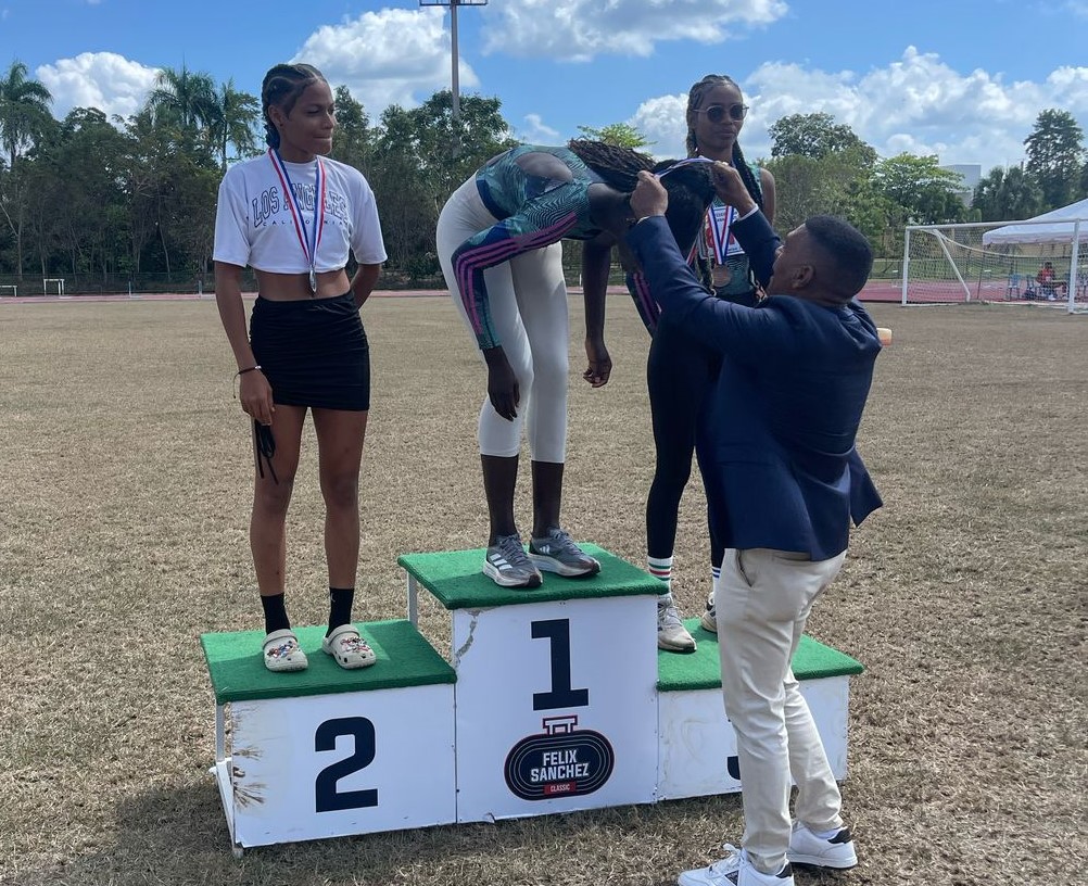 El presidente de la Federación de Atletismo, ingeniero Alexis Peguero, coloca la medalla a Marysabel Senyú que ganó oro en salto alto.