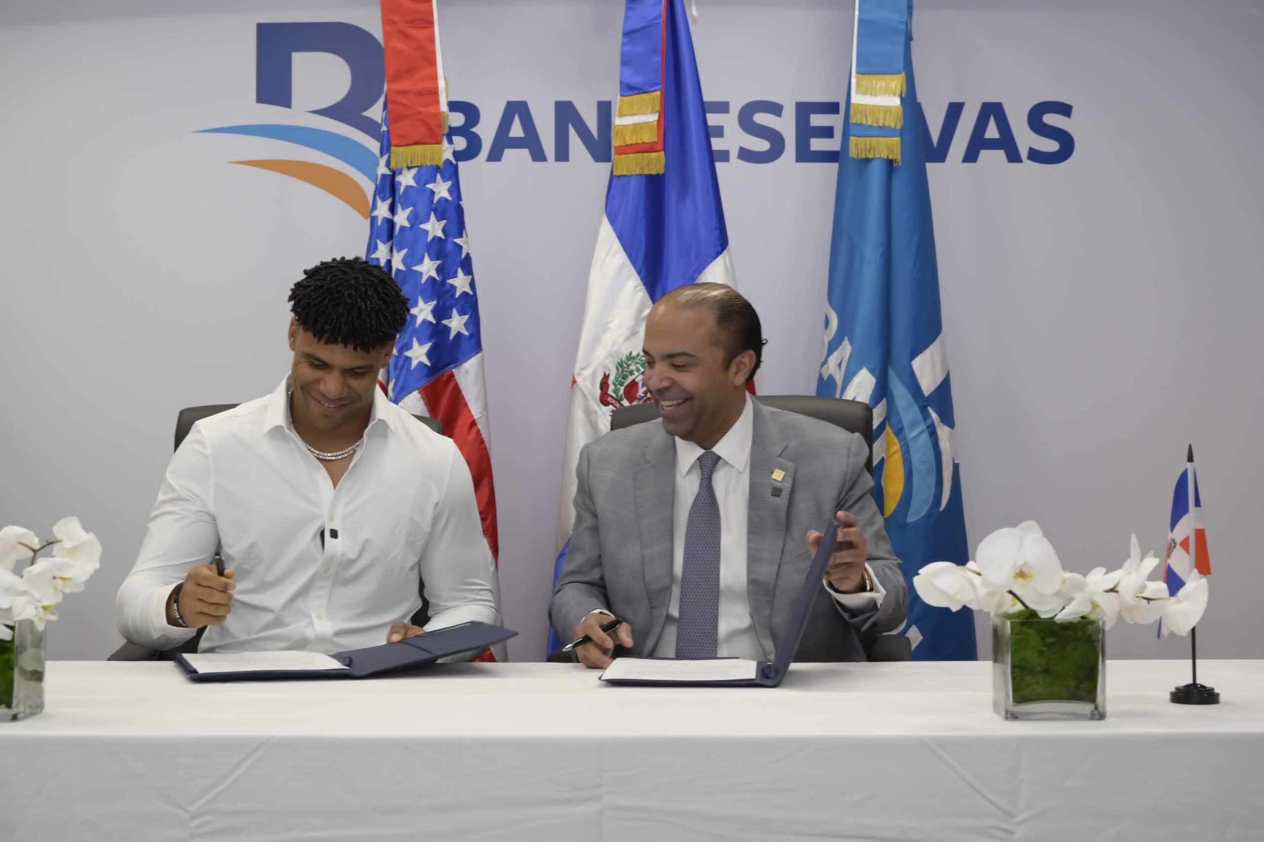 Samuel Pereyra, presidente ejecutivo de Banreservas y la super estrella del beisbol de Grandes Ligas, Juan Soto, firman el acuerdo para promover la dominicanidad durante un acto en la oficina de representación de la entidad bancaria en New York.