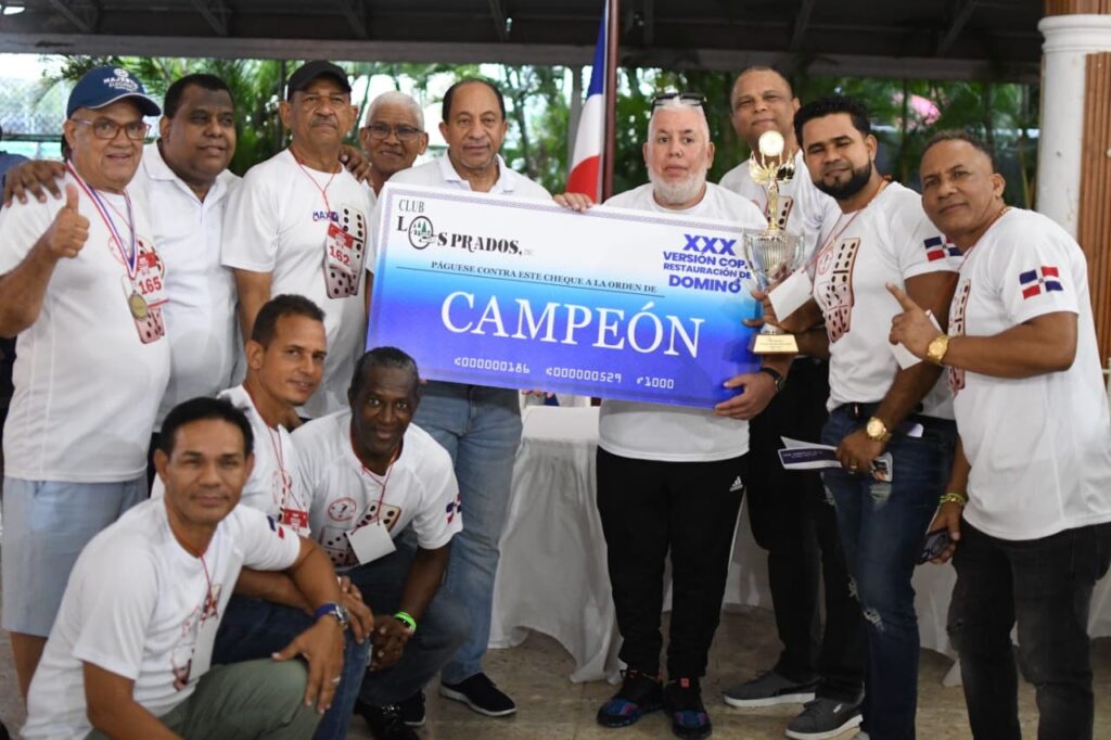 Jorge Ramírez, presidente del club Los Prados, entrega la Copa Restauración de Dominó al equipo campeón del Grupo 1, «Conoce Tú País», de La Romana, junto a Héctor Junior Gil.