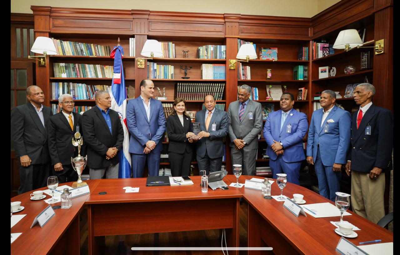 La vicepresidenta Raquel Peña recibe un reconocimiento de Jorge Ramírez, presidente del Club Los Prados, por la dedicatoria de la Copa Restauración de Dominó. Desde la izquierda, Pedro Pablo Rosario, Luis Tejeda, Luis Rieca, Adolfo Pérez, Héctor Junior Gil, Aleksey Ramírez, Benjamín Morales y Frank Féliz Puente.