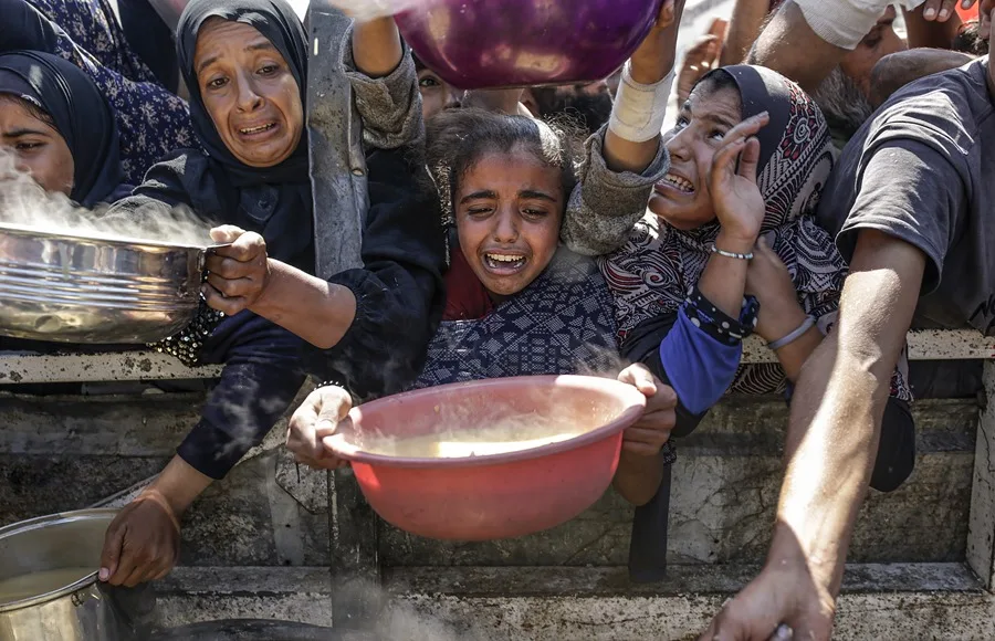 Palestinos desplazados internos, incluidos niños, sostienen ollas mientras se reúnen para recibir comida de un comedor social en la ciudad de Gaza.