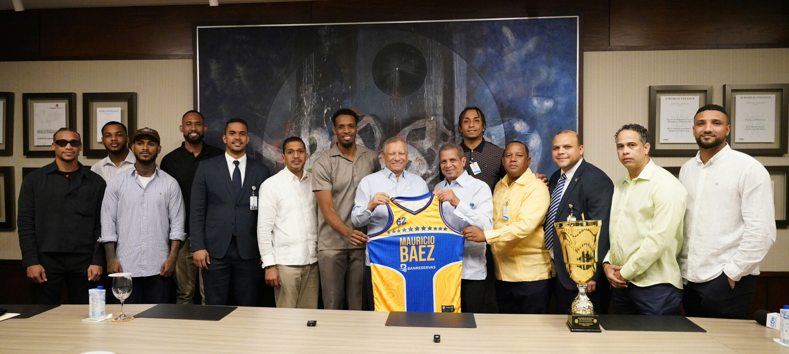 El presidente ejecutivo del Banreservas, Leonardo Aguilera, recibe la chaqueta oficial del Mauricio Báez, de parte de Leo Corporán,  presidente fundador de la Fundación Mauricio Báez; Gerardo Suero, capitán del equipo y Melvyn López, entrenador. Desde la izquierda figuran Pavel John Domínguez, Eduardo Mejía, Danilo Núñez, Eduardo Pereyra, Diego Moquete, César Heredia, Shamil Ballas, Amaury Heredia, Ruddy Martínez y Juan Heredia Pichardo.