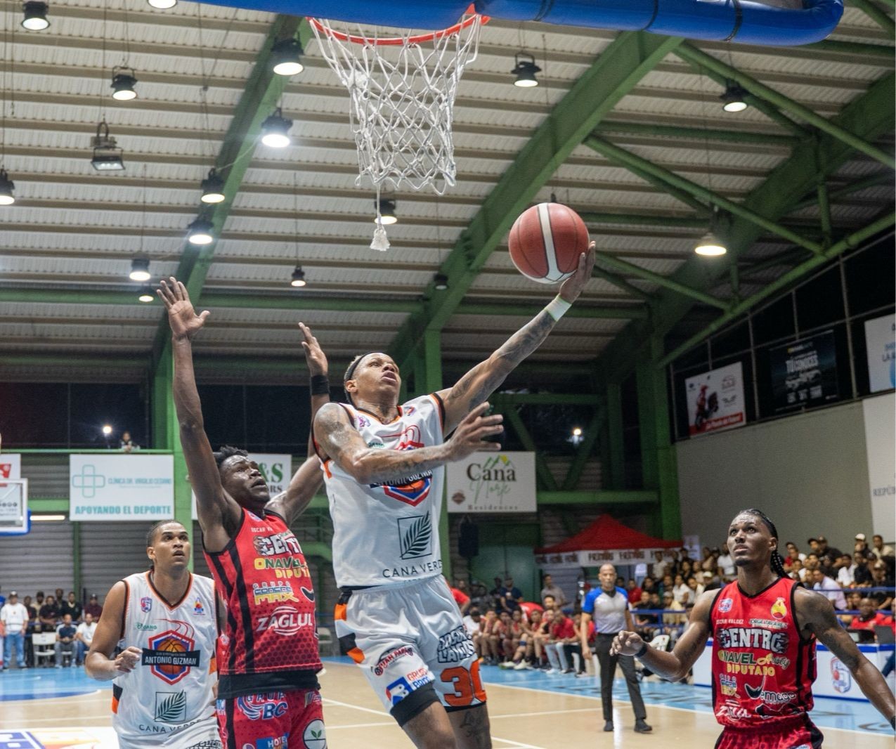 Oliver García, del club Antonio Guzmán, saca su izquierda para completar la anotación ante los defensas Nathanael Louis y Jordy Peralta del club Centro.