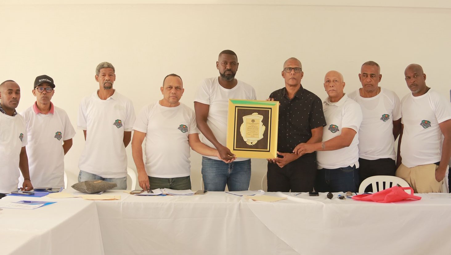 William Cabral Lugo, presidente de Abasado, reconoce a Mariano Linares, en nombre del fenecido Candelario Hidalgo, en la Asamblea Anual Ordinaria de Clubes 2026. Le acompañan, desde la izquierda, Valentín Ozuna, Domingo De la Rosa, Ramón Guzmán, Agustín Matos, Luis Pimentel, José Esteban Borromé y Juan Carlos Medina (Negrura).