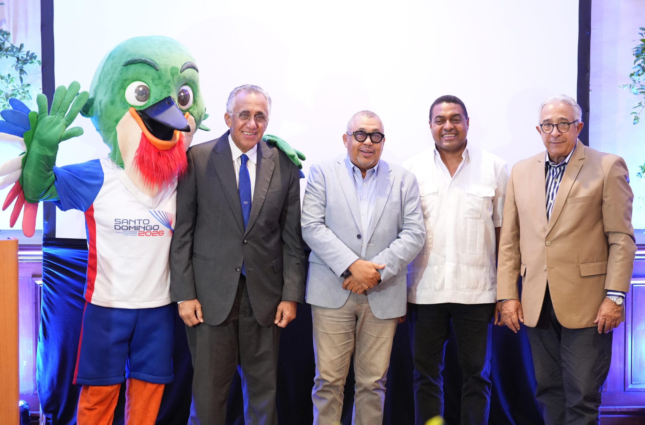 Colí, la mascota de los Juegos Centroamericanos y del Caribe Santo Domingo 2026 junto a Luisín Mejía, Américo Celado, José P. Monegro y Dionisio Guzmán.