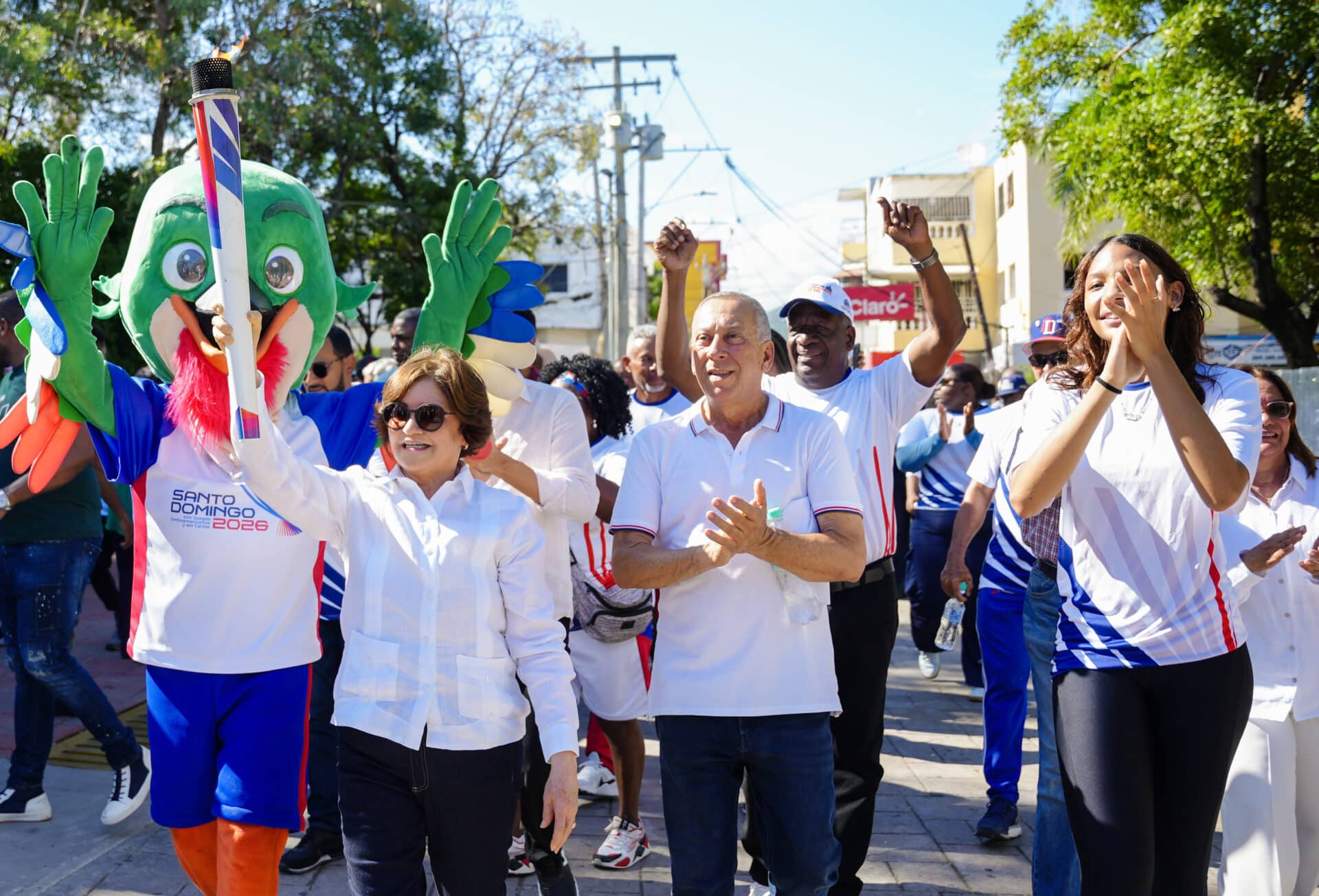 La gobernadora de Baní, Ángela Yadhira Báez, camina portando la antorcha de los Juegos Santo Domingo 2026, durante un tramo del recorrido en esa localidad.