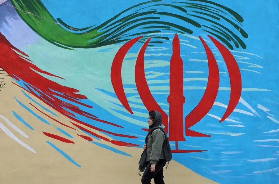 Fotografía de archivo de una mujer caminando frente a un mural con la bandera iraní, en Teherán (Irán). EFE/ Abedin Taherkenareh.