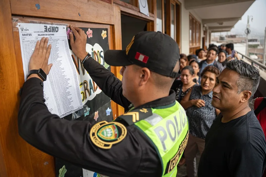 Un integrante de la Policía pega un cartel afuera de un aula de votaciones en el colegio Señor de los Milagros, en el distrito de Lurín (Perú). EFE/ John Reyes Mejía.