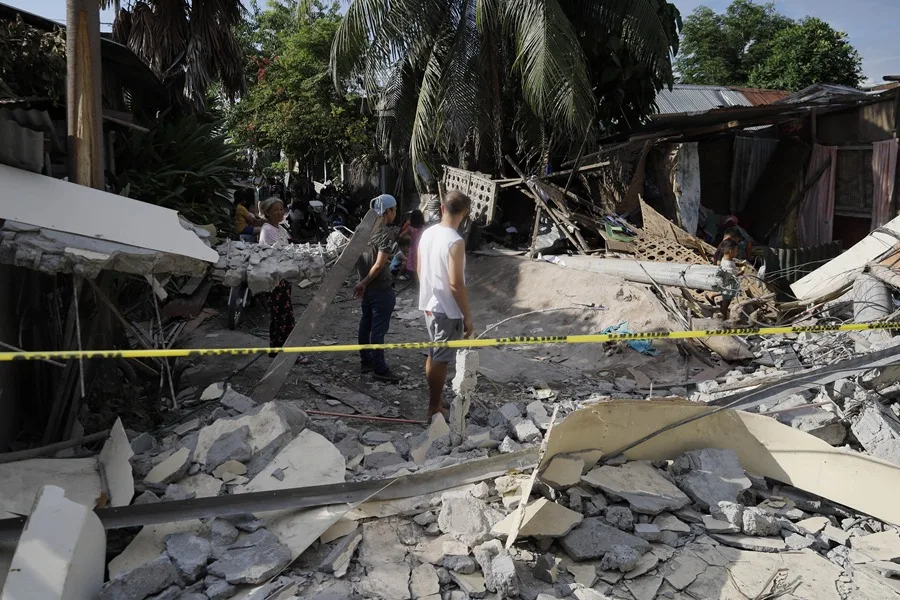 Varias personas inspeccionan los daños en el lugar donde se ha derrumbado un muro que separaba unas instalaciones tipo almacén de varias viviendas, un día después del terremoto, en la ciudad de General Santos, al sur de Filipinas. EFE/EPA/Cerilo Ebrano.