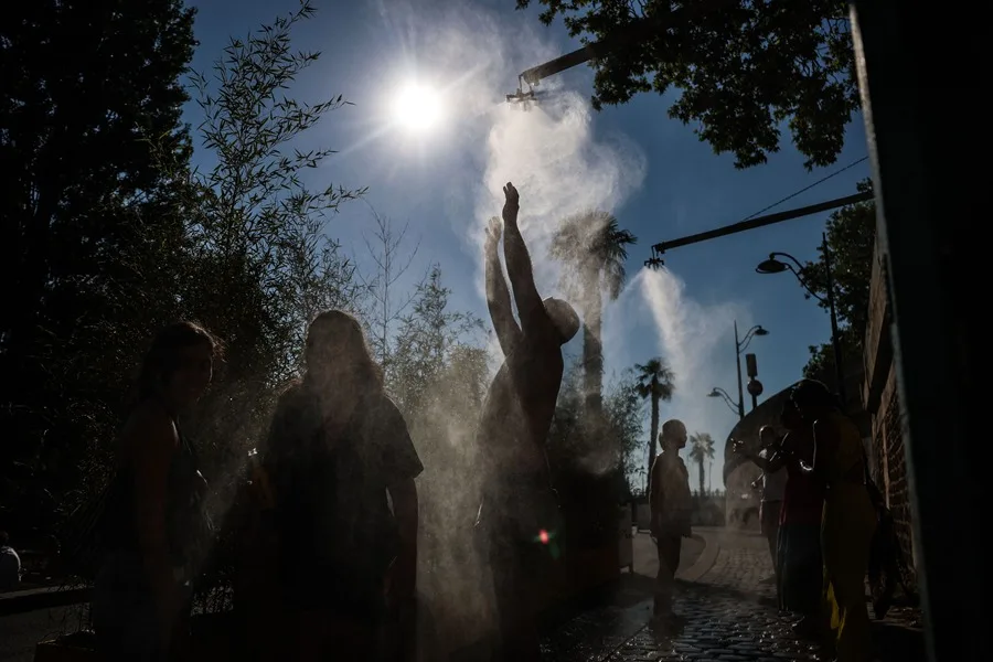 Personas caminan entre dispositivos que rocían agua pulverizada a orillas del Sena durante la ola de calor en París. EFE/EPA/Mohammed Badra.